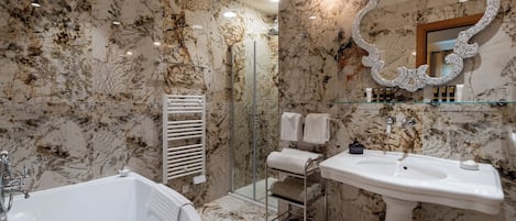 A bathroom with a marble wall, a freestanding bathtub, a pedestal sink, a glass shower enclosure, and a vanity with a mirror.