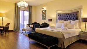 A hotel room with a large bed, a bench, a chair, a desk, and a chandelier. - Demeure Loredana  (Saint-Florent)
