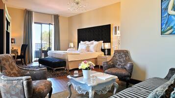 Une chambre d’hôtel avec un grand lit, deux fauteuils, un canapé, une table basse ornée d’un vase de fleurs, un lustre et un tableau accroché au mur.