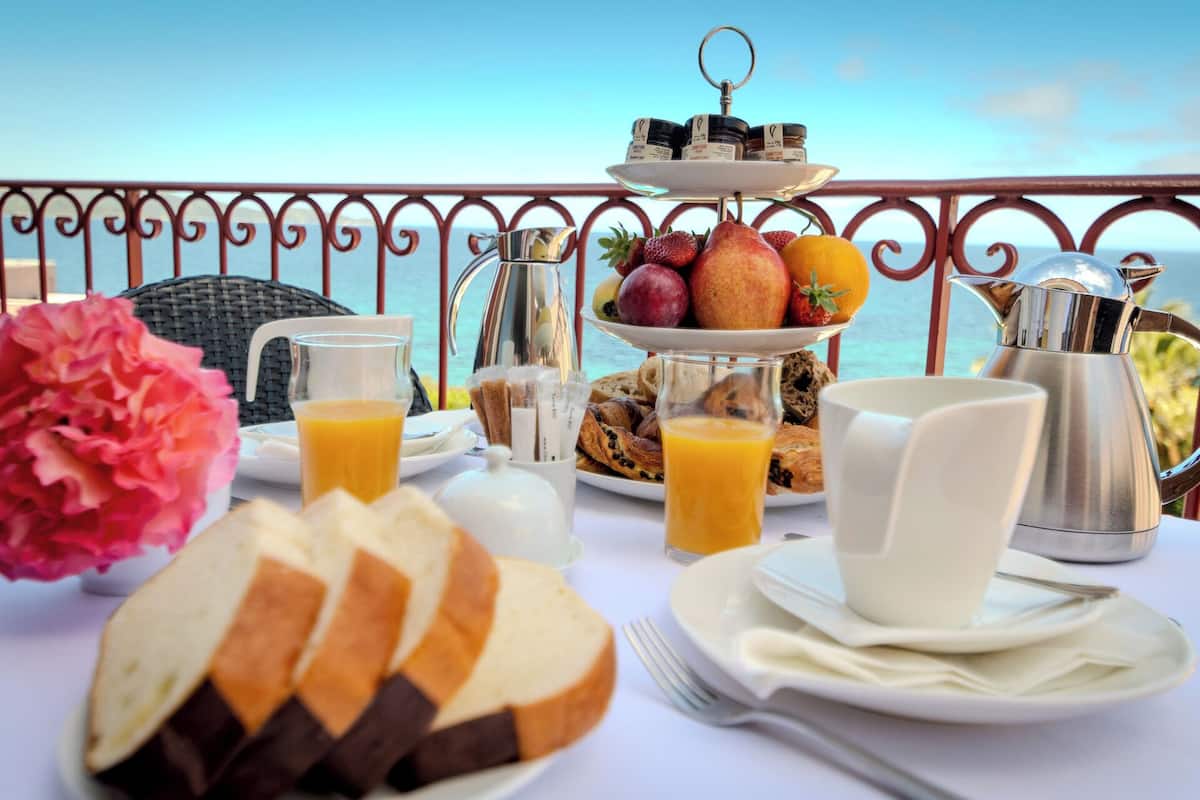 Un buffet de petit-déjeuner avec des viennoiseries, des fruits et des boissons, installé sur un balcon donnant sur la mer.
