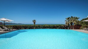 A clear blue pool with lounge chairs and umbrellas, surrounded by greenery and a view of the sea. - Demeure Loredana  (Saint-Florent)