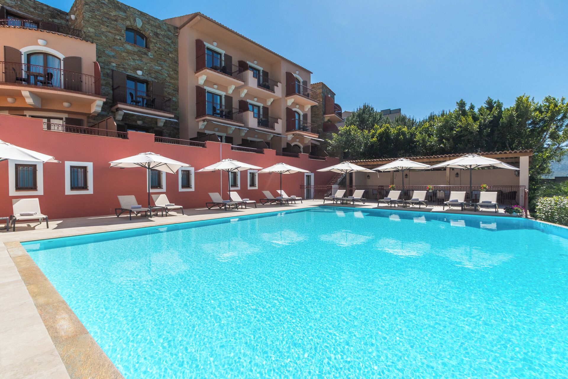 Una piscina con sillones de descanso y sombrillas, rodeada de edificios con balcones y ventanas.