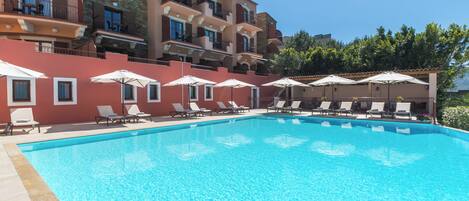 Una piscina con sillones de descanso y sombrillas, rodeada de edificios con balcones y ventanas.