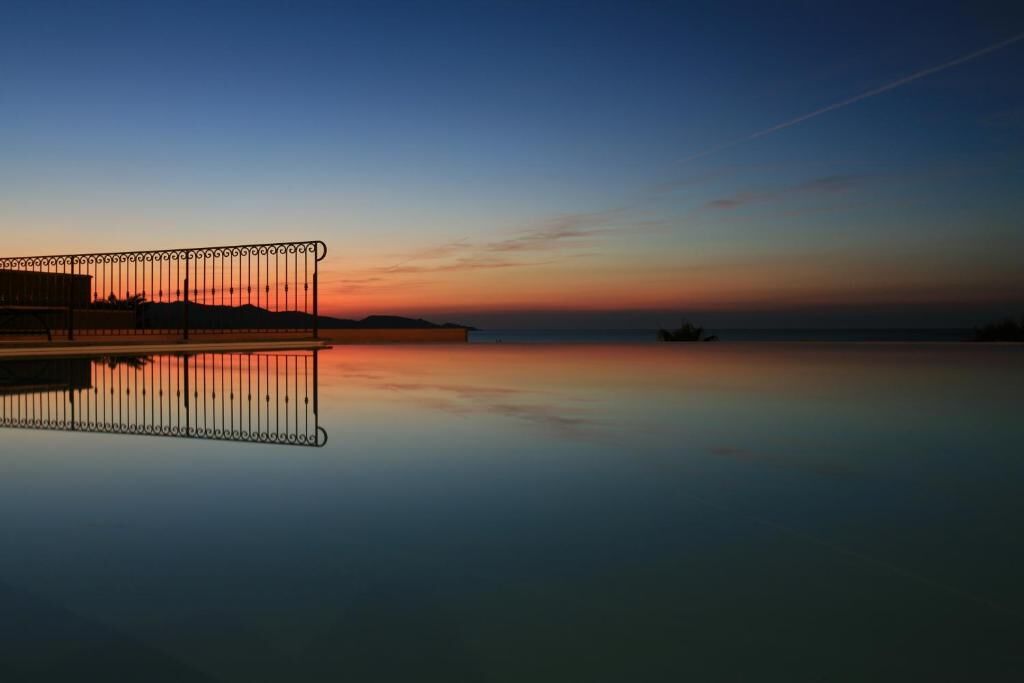 A calm waterfront at sunset with a metal railing and a distant boat.