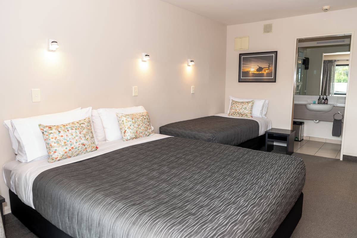 A hotel room with two beds, a bathroom with a sink, and a mirror.