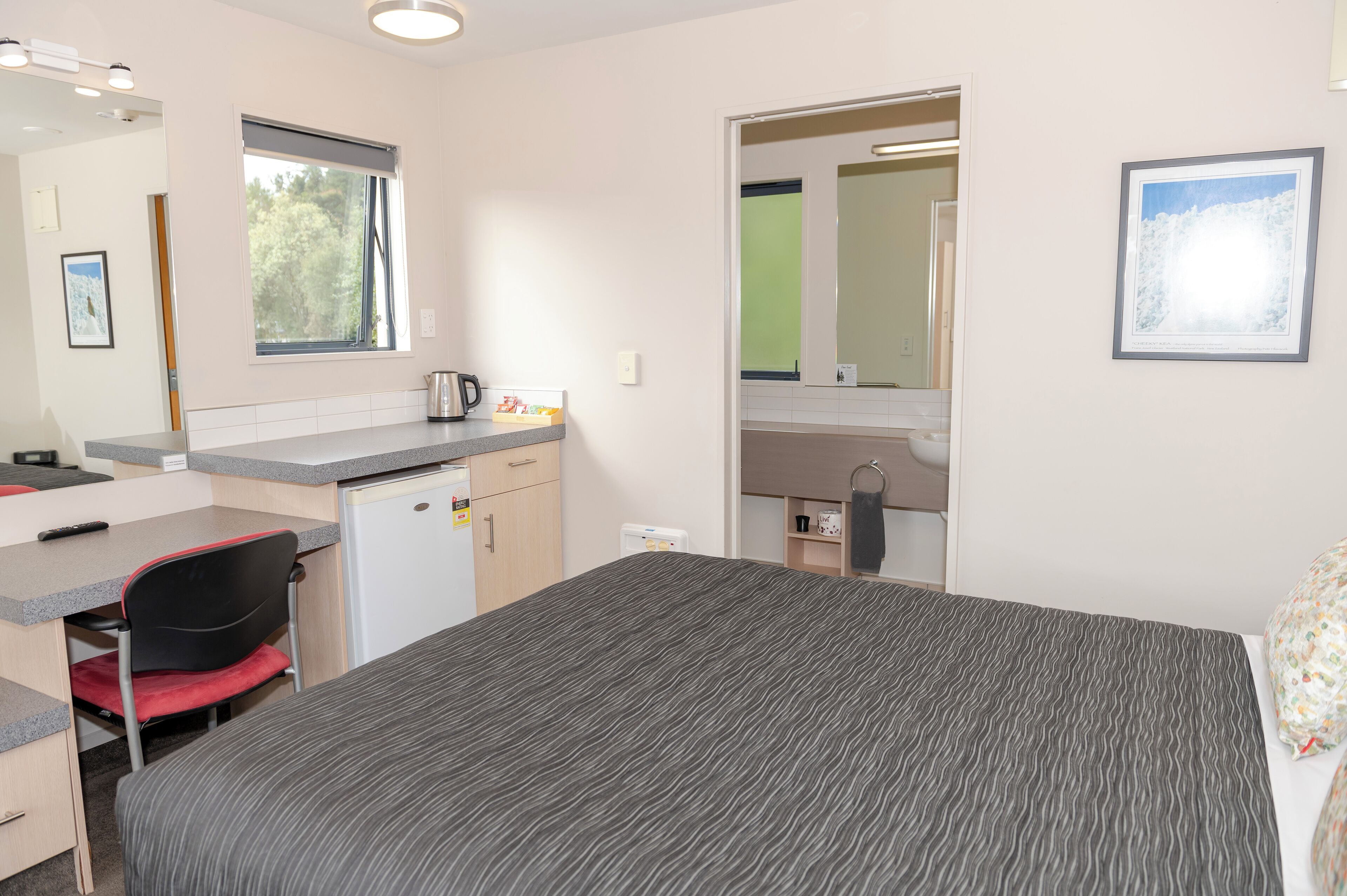A compact room with a bed, a desk, a chair, a kitchenette, and a bathroom.
