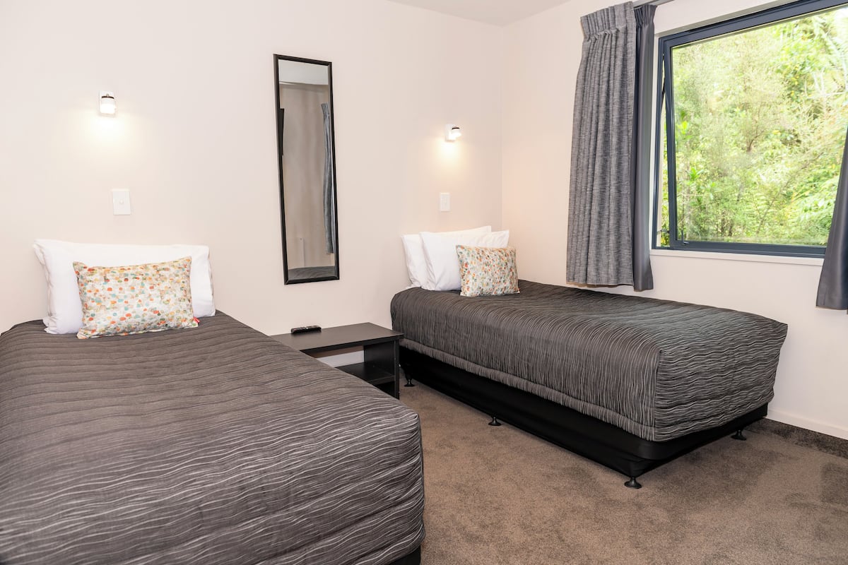A room with two beds, a mirror, a window with curtains, and a small table.