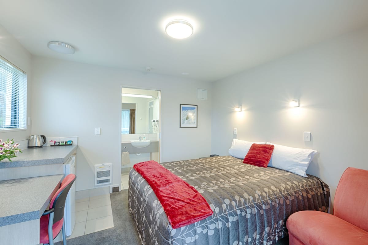A hotel room with a bed, a desk, a chair, a sink, and a mirror.