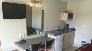 Una kitchenette compacta con microondas, lavamanos y refrigerador pequeño. Hay una zona de comedor con dos sillas y una mesa.