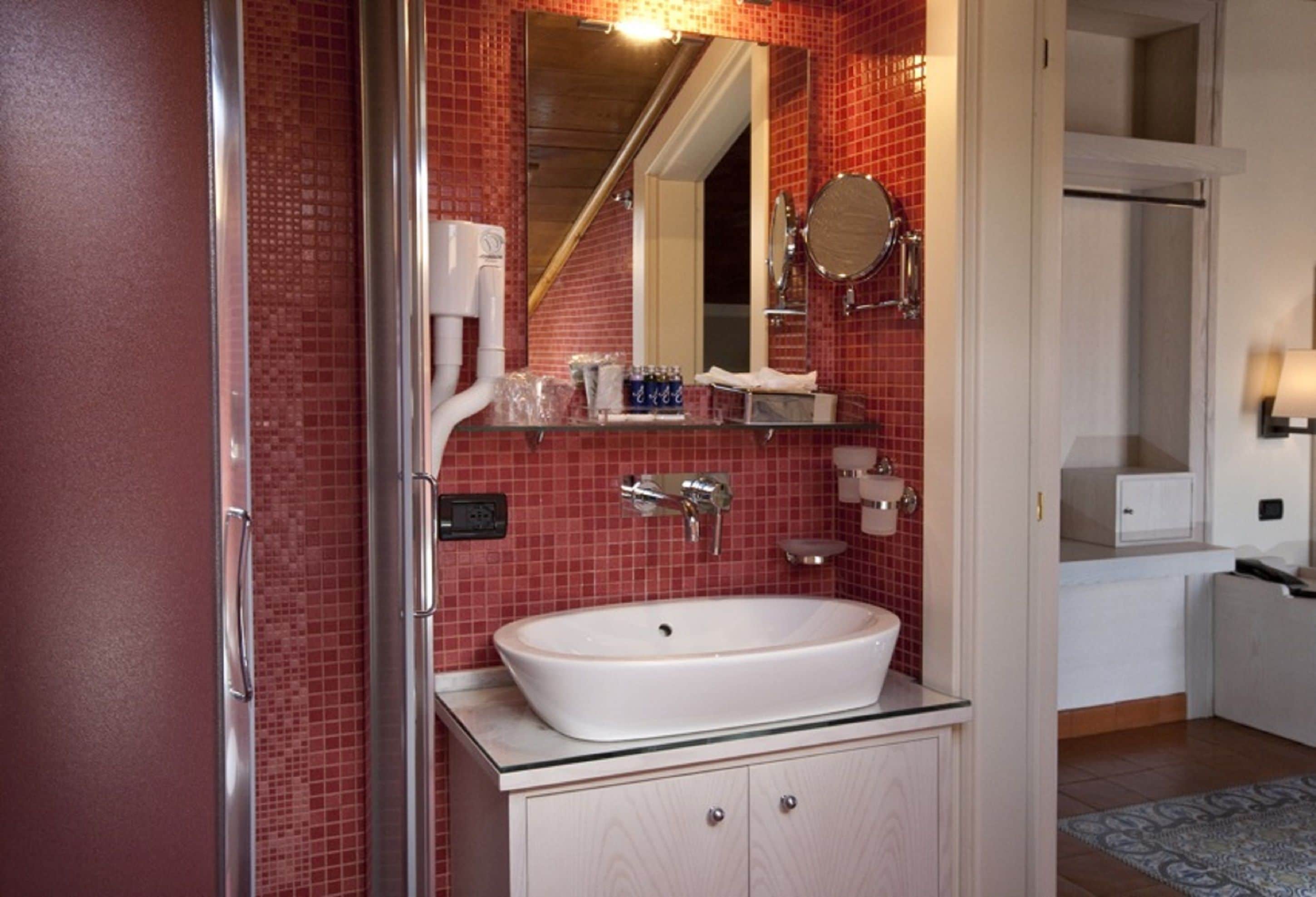 A bathroom with a white sink, red tiled walls, a mirror, and a glass shower enclosure.