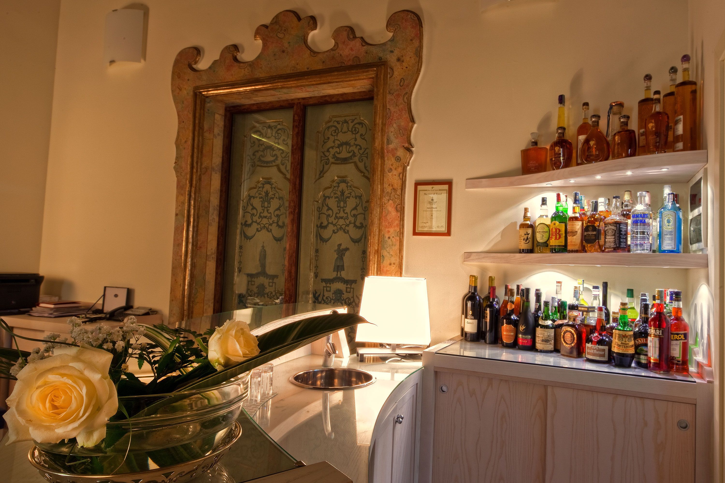 A bar area with a variety of liquor bottles, a glass bowl with flowers, and a decorative mirror.