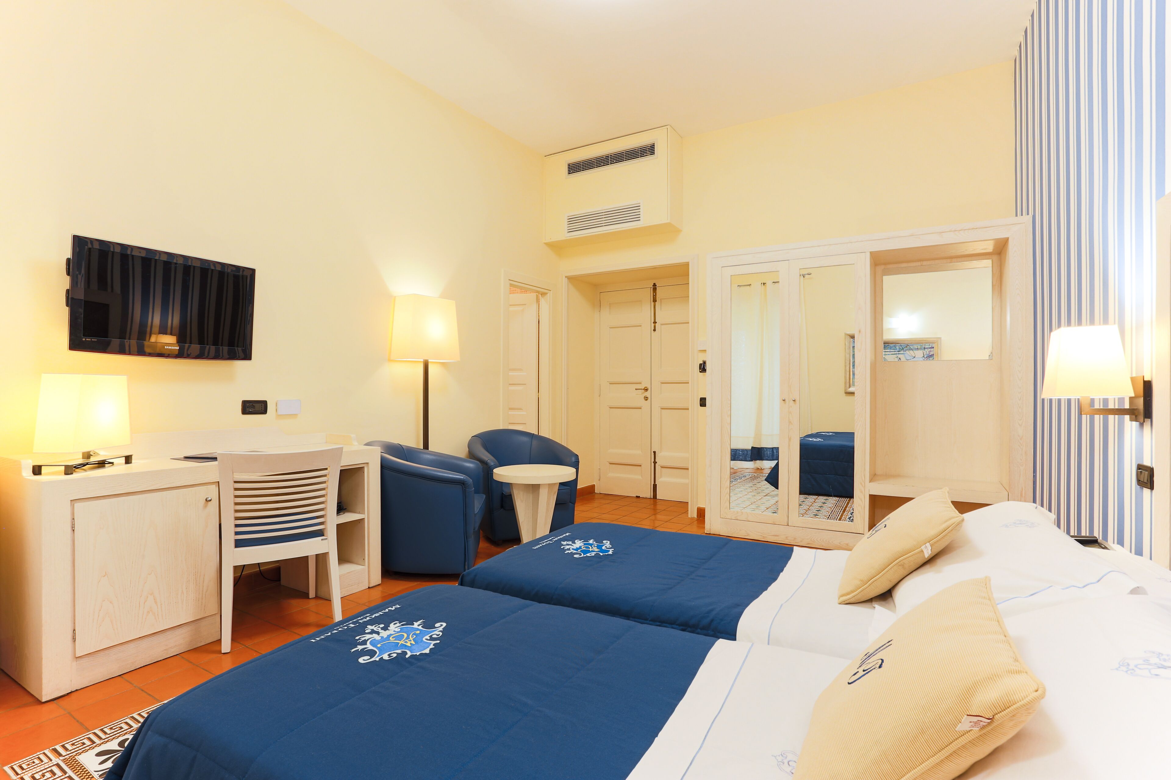 A hotel room with two beds, a desk, a chair, a small table, and a mirror.