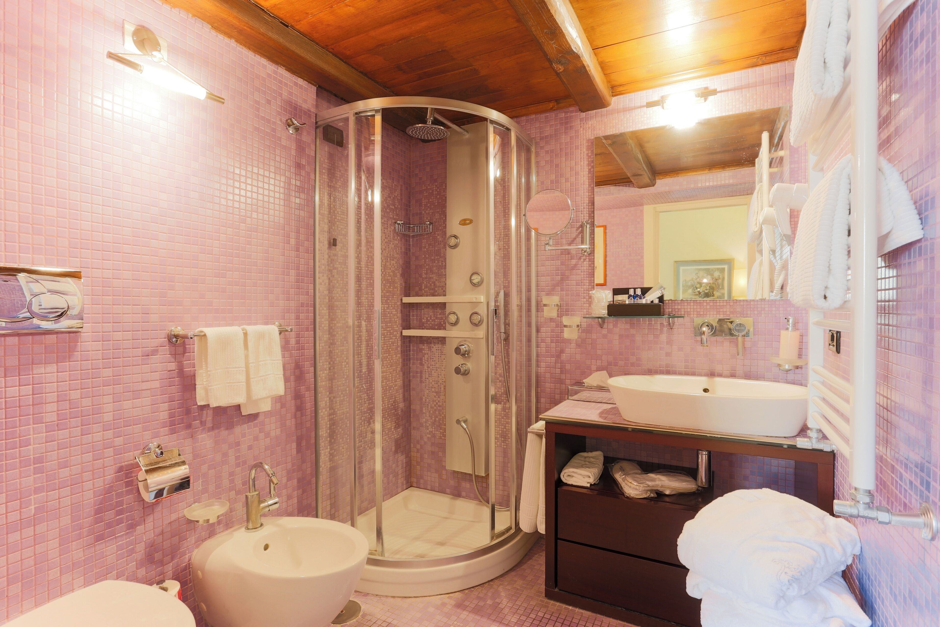 A bathroom with pink tiled walls, a glass-enclosed shower, a sink, and a mirror.