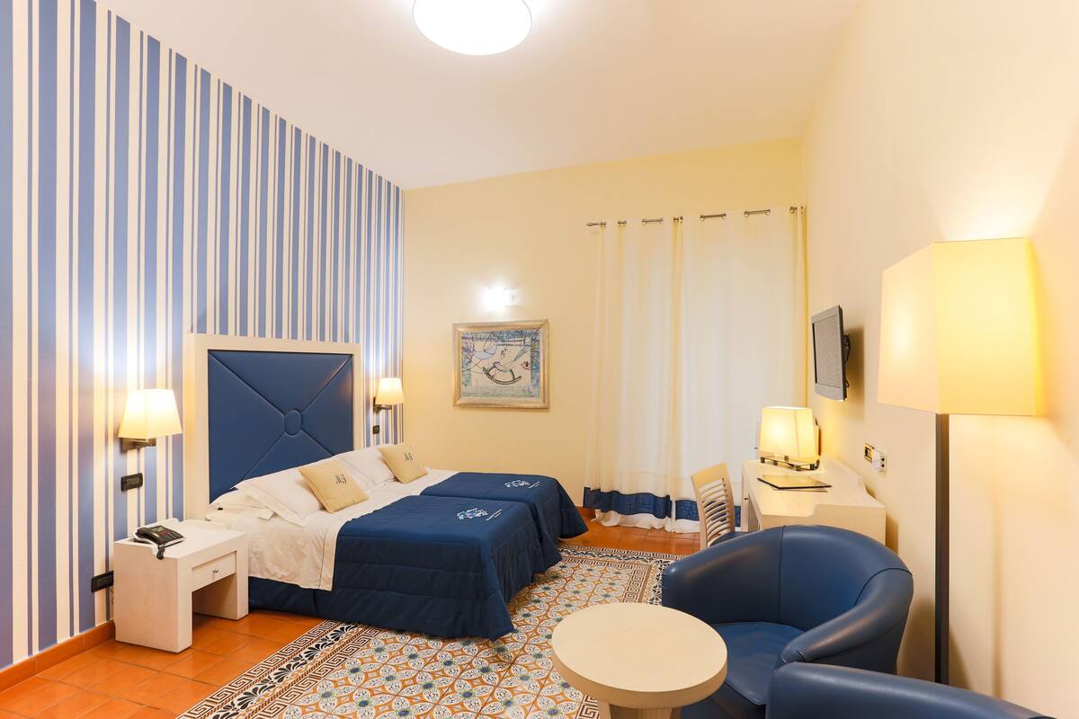 Ett hotellrum med två sängar, ett skrivbord, en stol och ett litet bord.