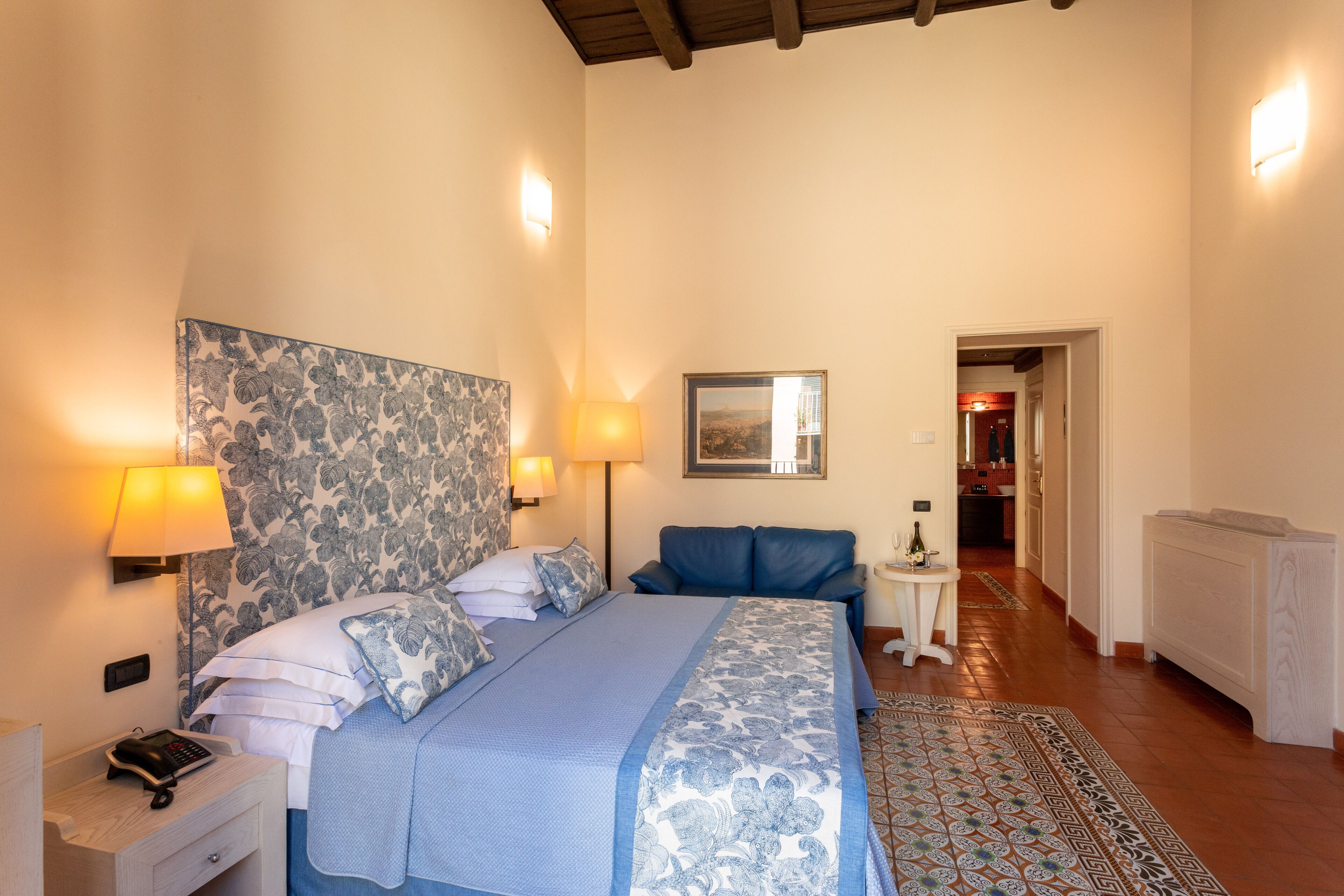 Un dormitorio con una cama grande, dos lámparas de noche, una mesita de noche, una pequeña mesa y una alfombra estampada.