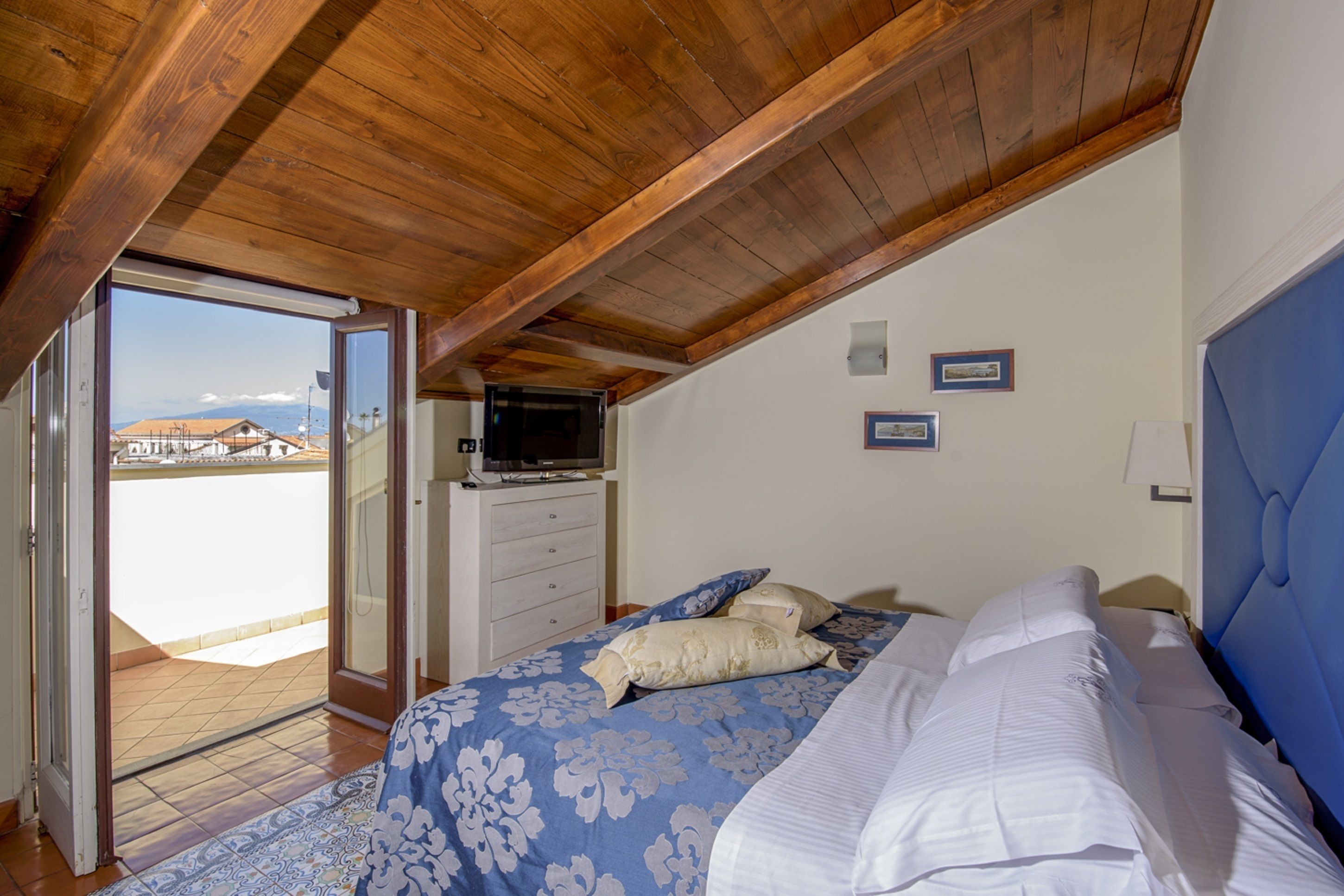 Een slaapkamer met een bed, een dressoir, een televisie en uitzicht op buiten.