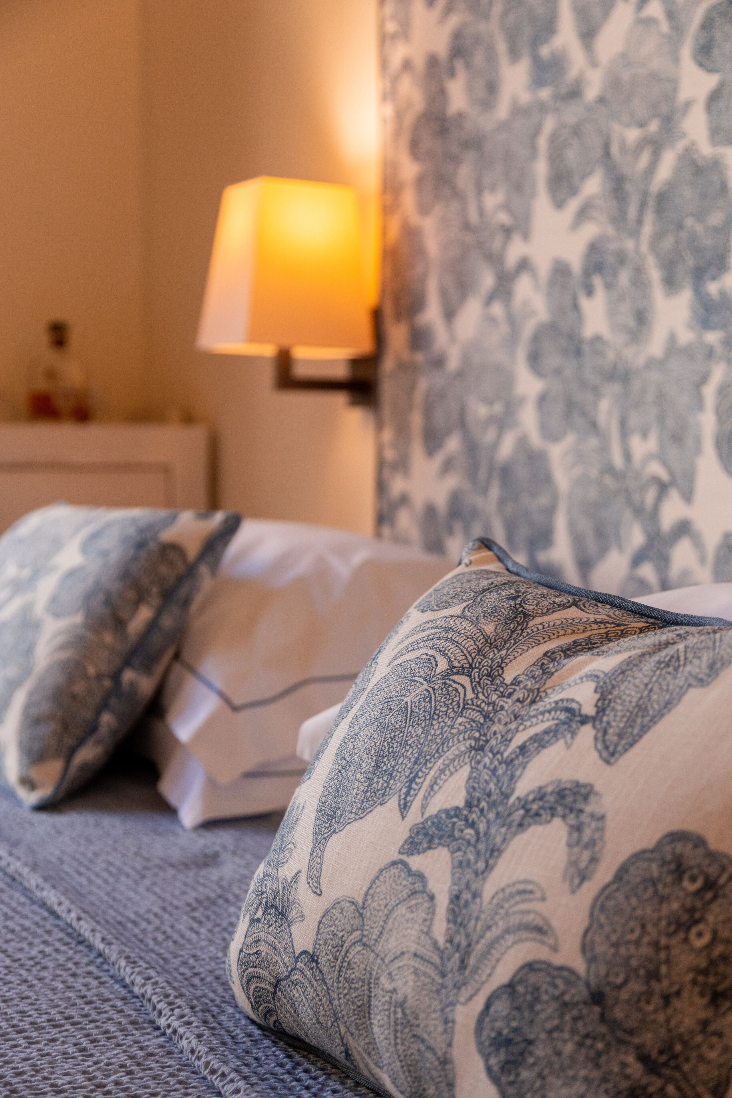 A bed with patterned pillows and a wall with a floral wallpaper.