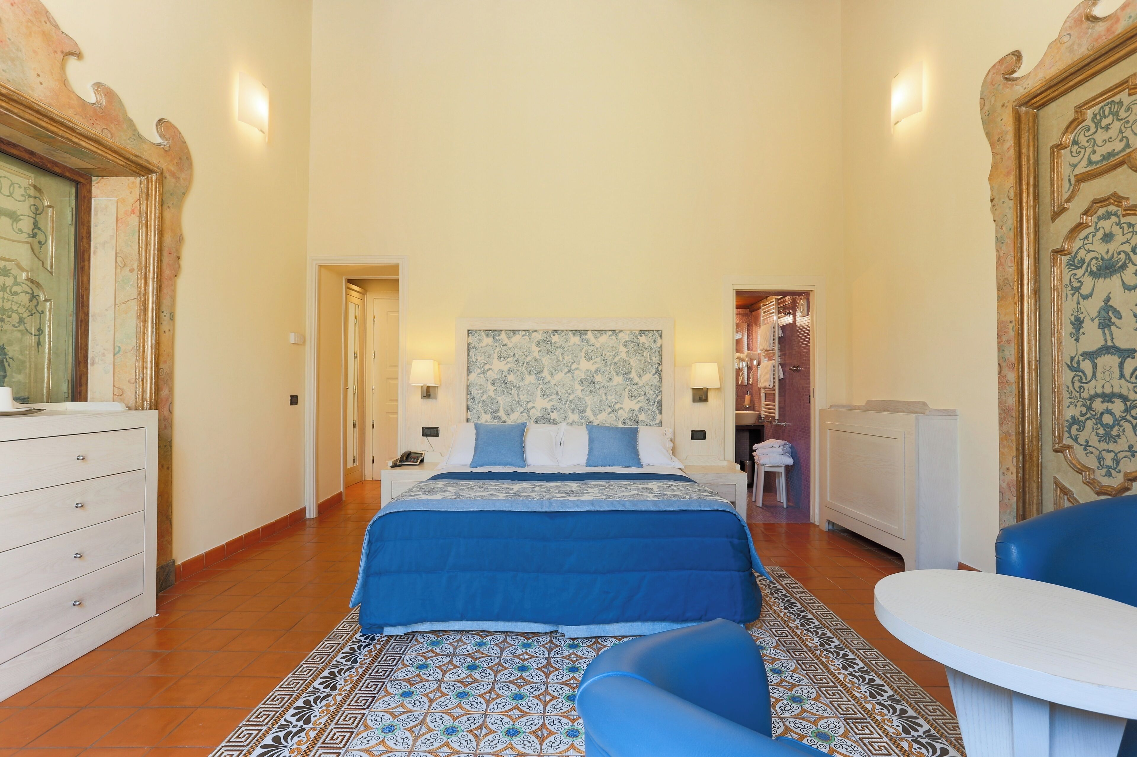 Una camera d'albergo con un letto grande, un tavolino, una sedia e una cassettiera.
