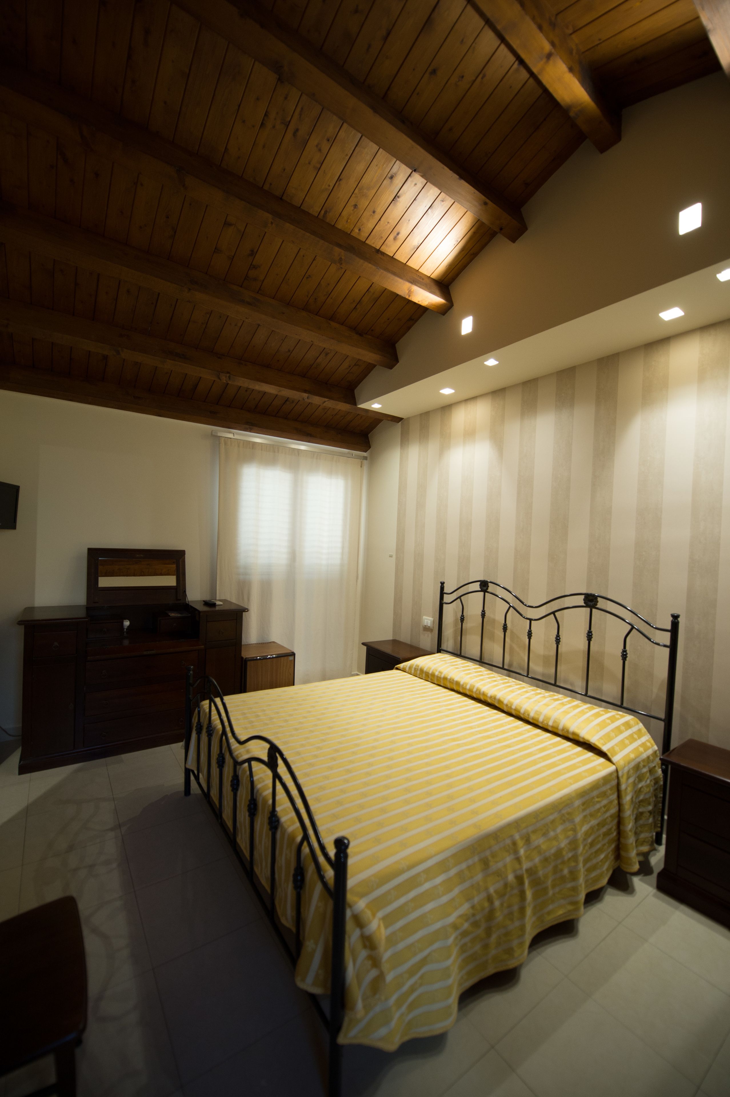 A bedroom with a wooden ceiling, a bed with a striped bedspread, a dresser, and a nightstand.