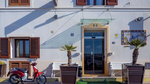 A hotel entrance with a glass door, a scooter parked outside, and two potted plants. - Hotel Aliai (Sciacca)