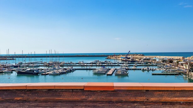 A marina with boats docked, a clear sky, and a distant shoreline. - Hotel Aliai (Sciacca)