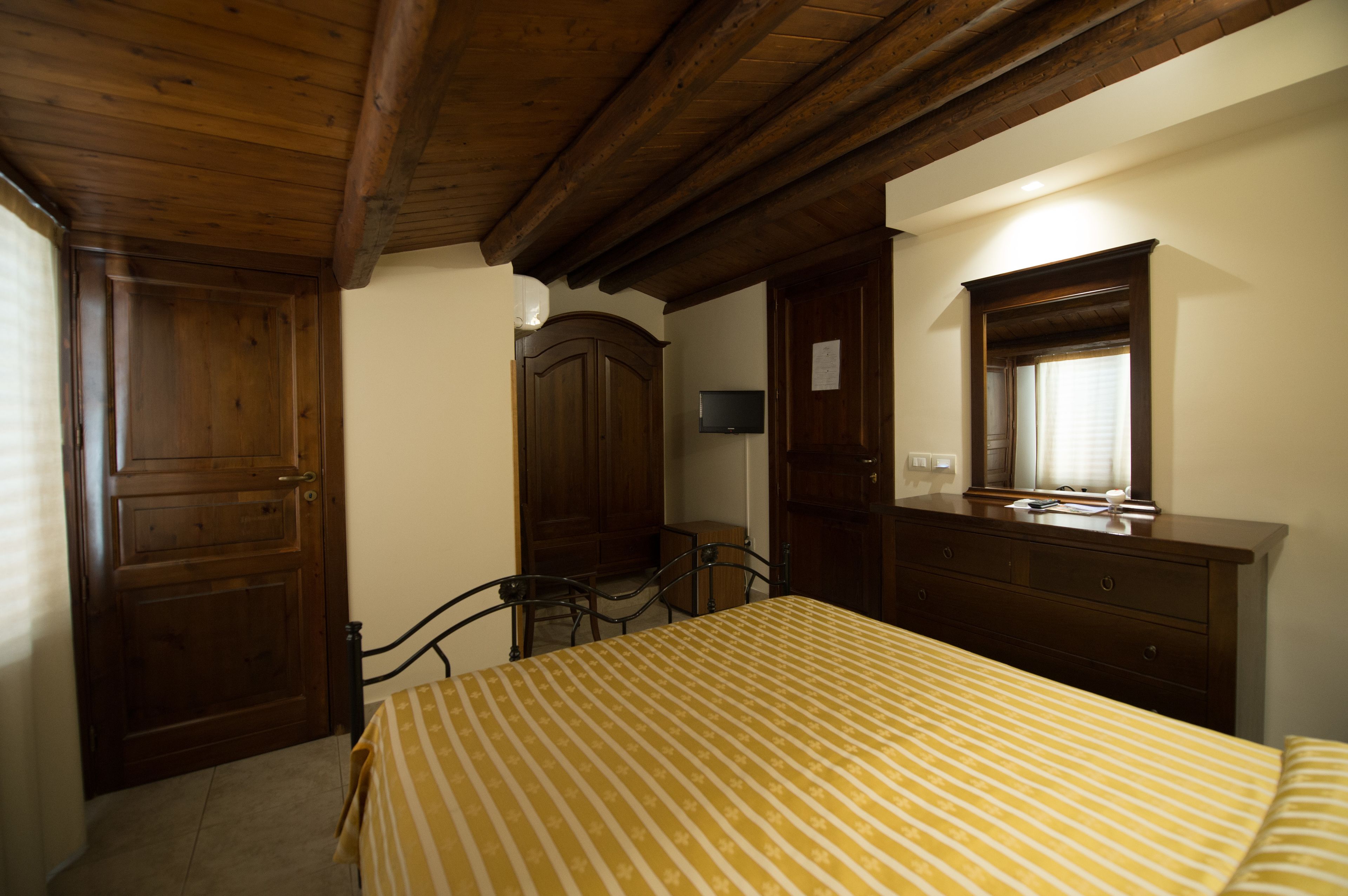 Een slaapkamer met een bed, een houten kledingkast, een spiegel en een televisie op een standaard.