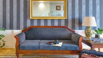 A room with a sofa, a mirror, a lamp, and a table with a vase.