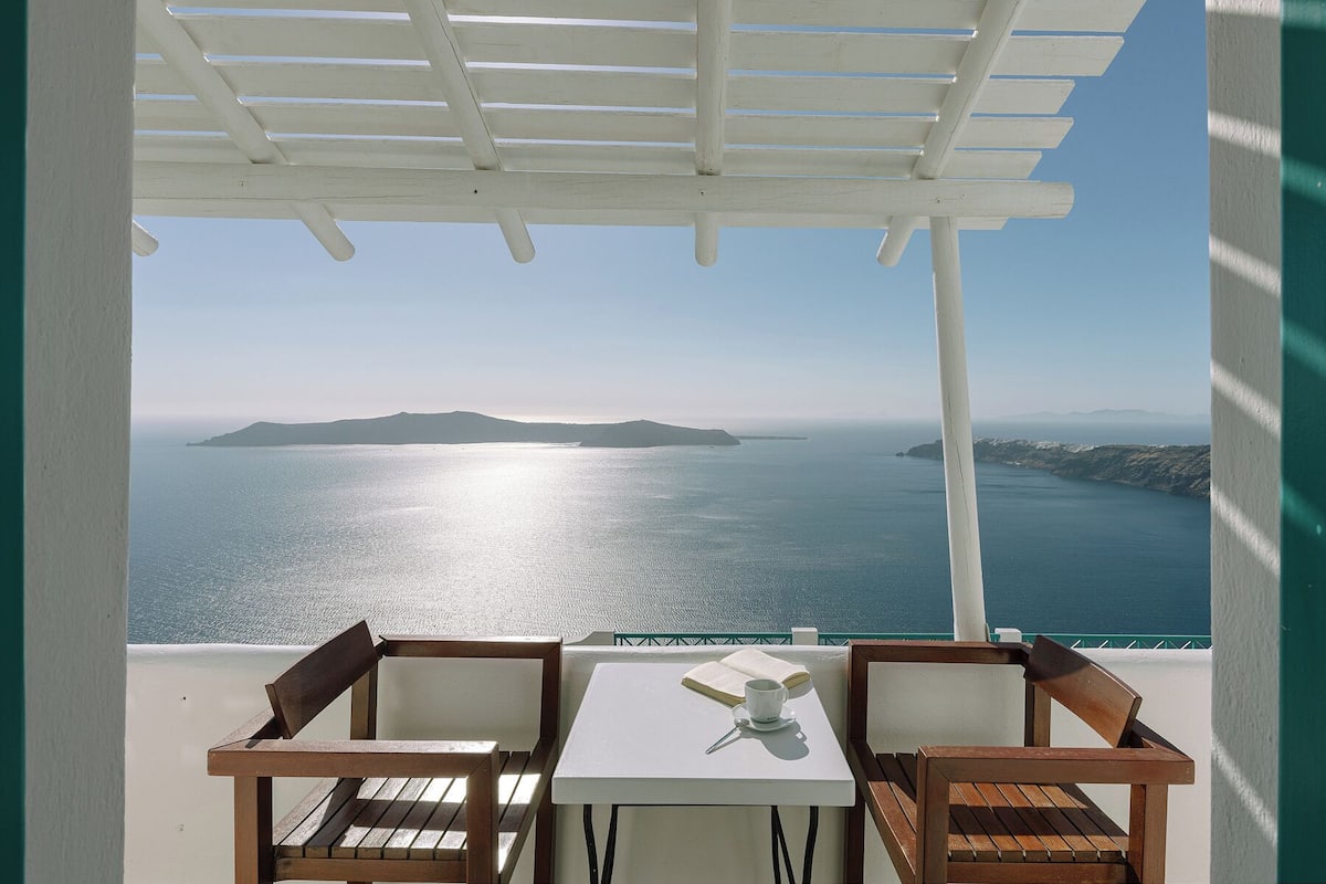 Un balcón con una mesa blanca, dos sillas de madera y vistas al mar y a las islas.