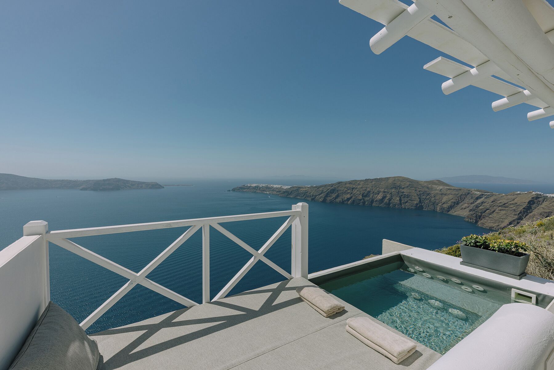 A pool with a view of the sea and mountains, a white railing, and a clear sky.