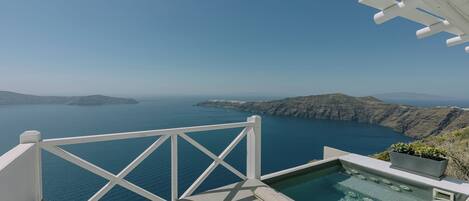 A pool with a view of the sea and mountains, a white railing, and a clear sky.