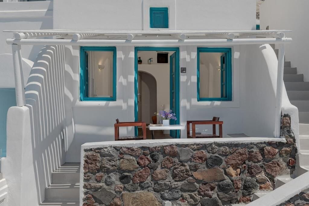 A white building with blue accents, a stone wall, and a staircase leading to an entrance.