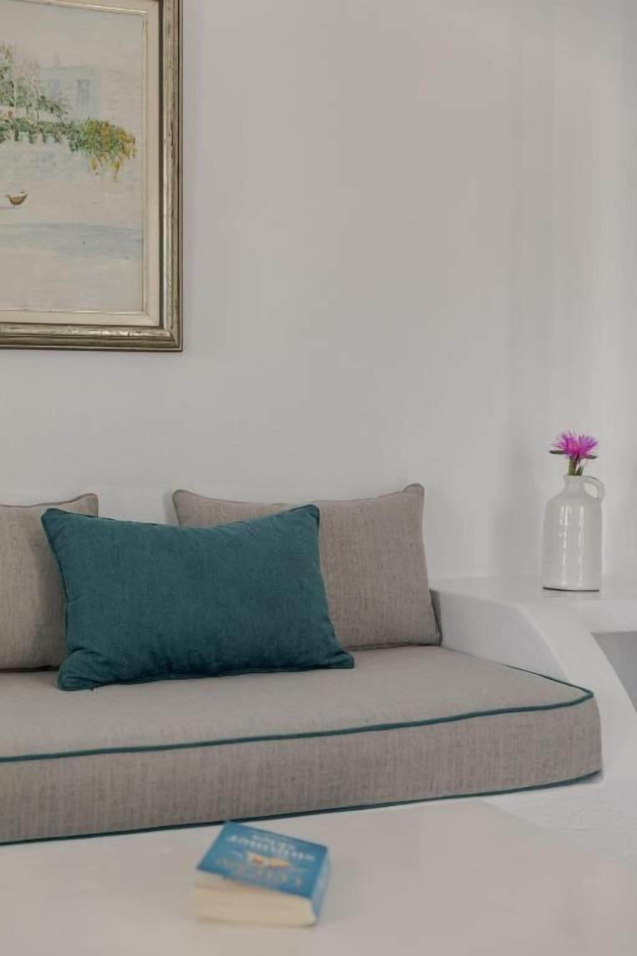 A modern living room with a sofa, pillows, a vase with flowers, and a framed picture on the wall.