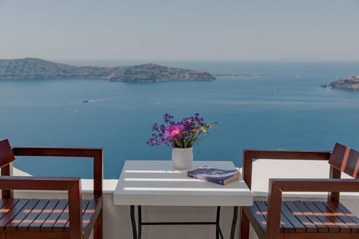 Una mesa con un jarrón de flores y un libro, dos sillas de madera, y vistas al mar y a las islas.