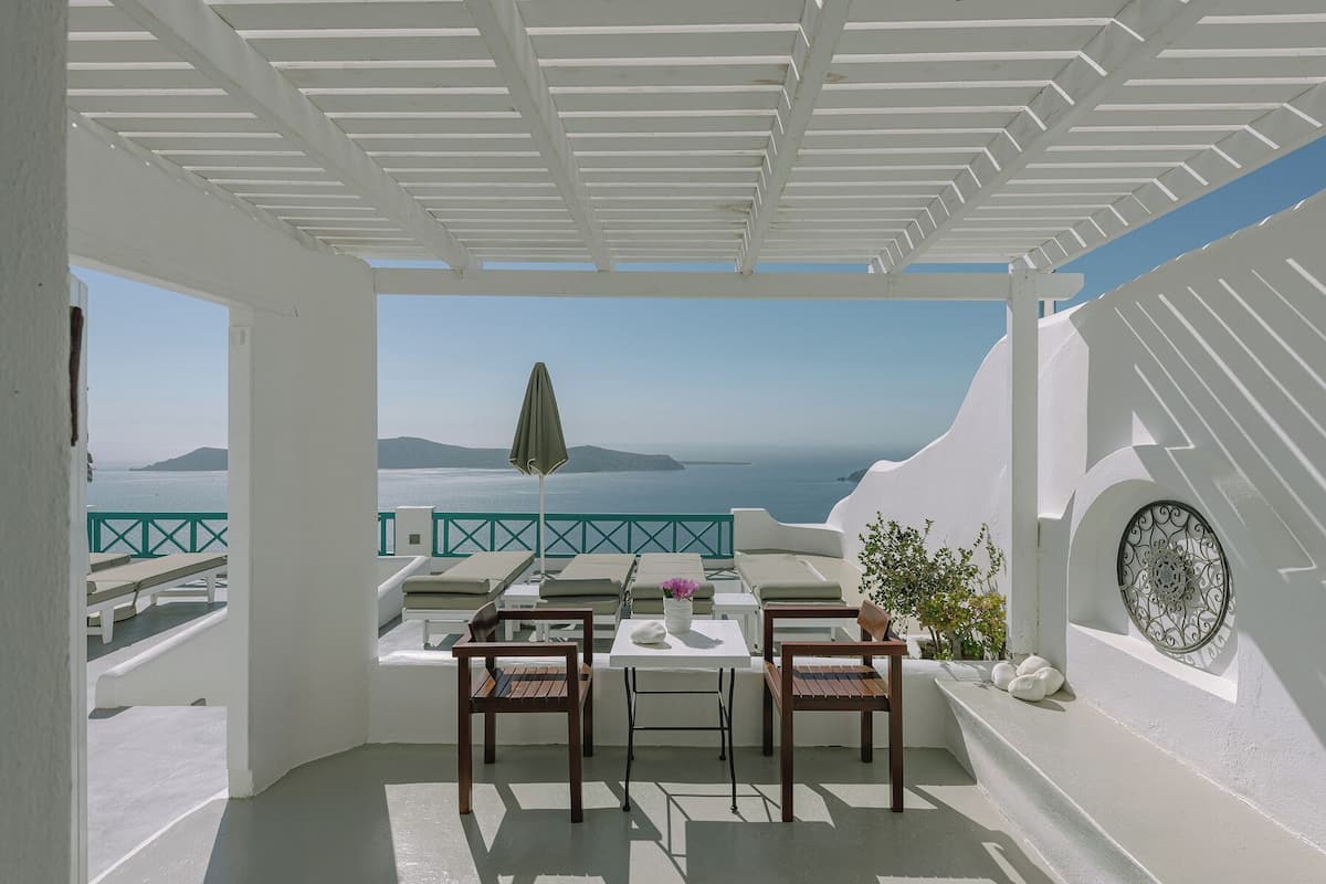 Una terraza con mesa y sillas, vista al mar y estilo arquitectónico blanco.