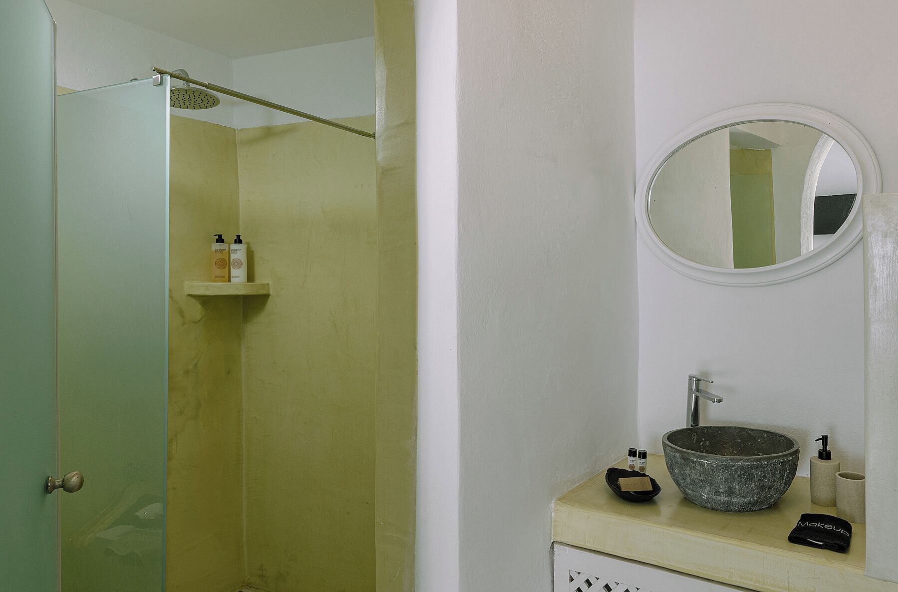 A bathroom with a shower, a sink with a stone basin, and toiletries on the counter.
