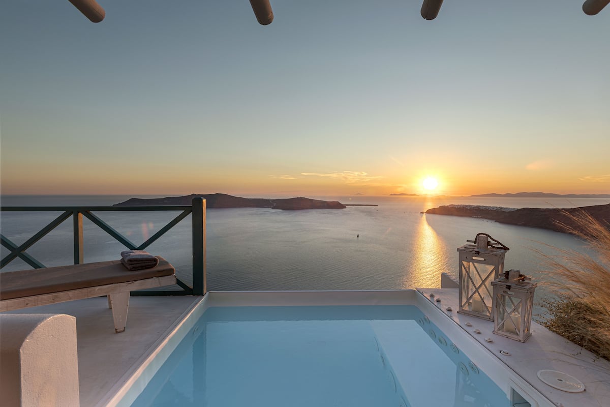 Un área de piscina con un banco de madera y faroles, con vistas al mar tranquilo al atardecer.