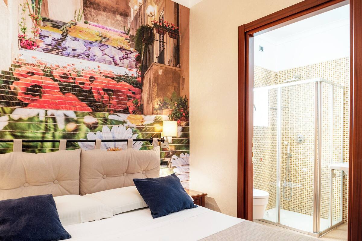 A hotel room with a large bed, a view of a balcony, and a mosaic wall.