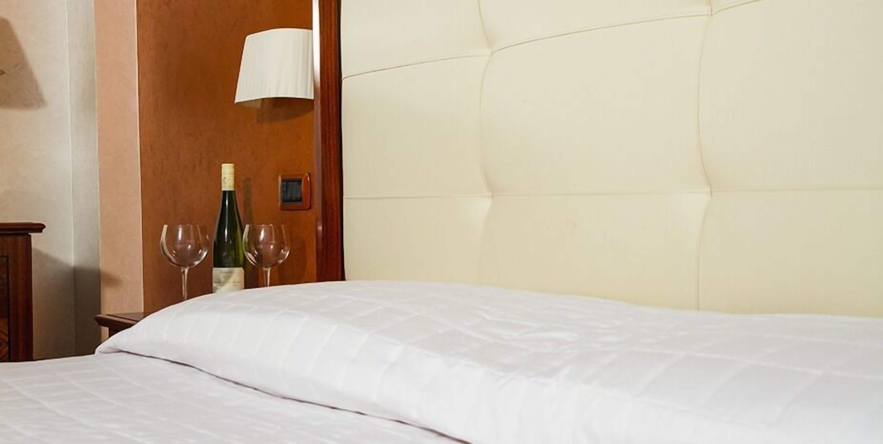 Ein Hotelzimmer mit einem großen Bett, einem Nachttisch aus Holz, einer Weinflasche und zwei Weingläsern.