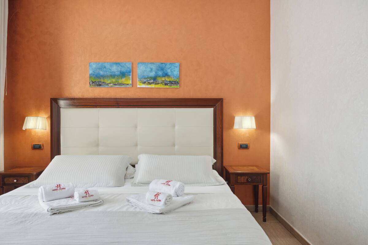 A hotel room with a large bed, two wall-mounted lamps, and two paintings above the bed.