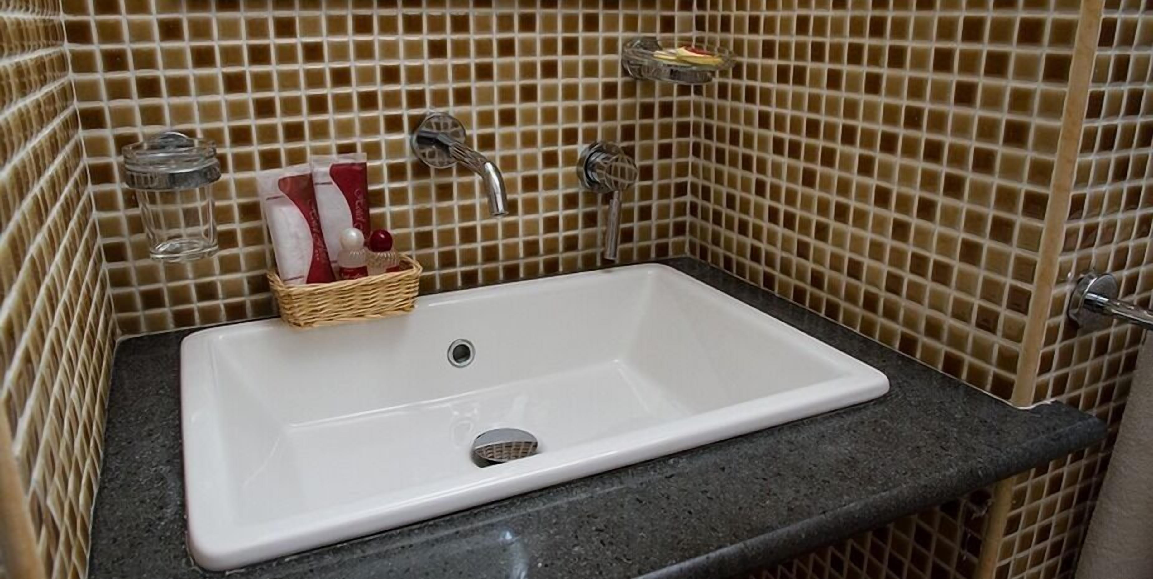 A bathroom with a white sink, two faucets, and a tiled backsplash.