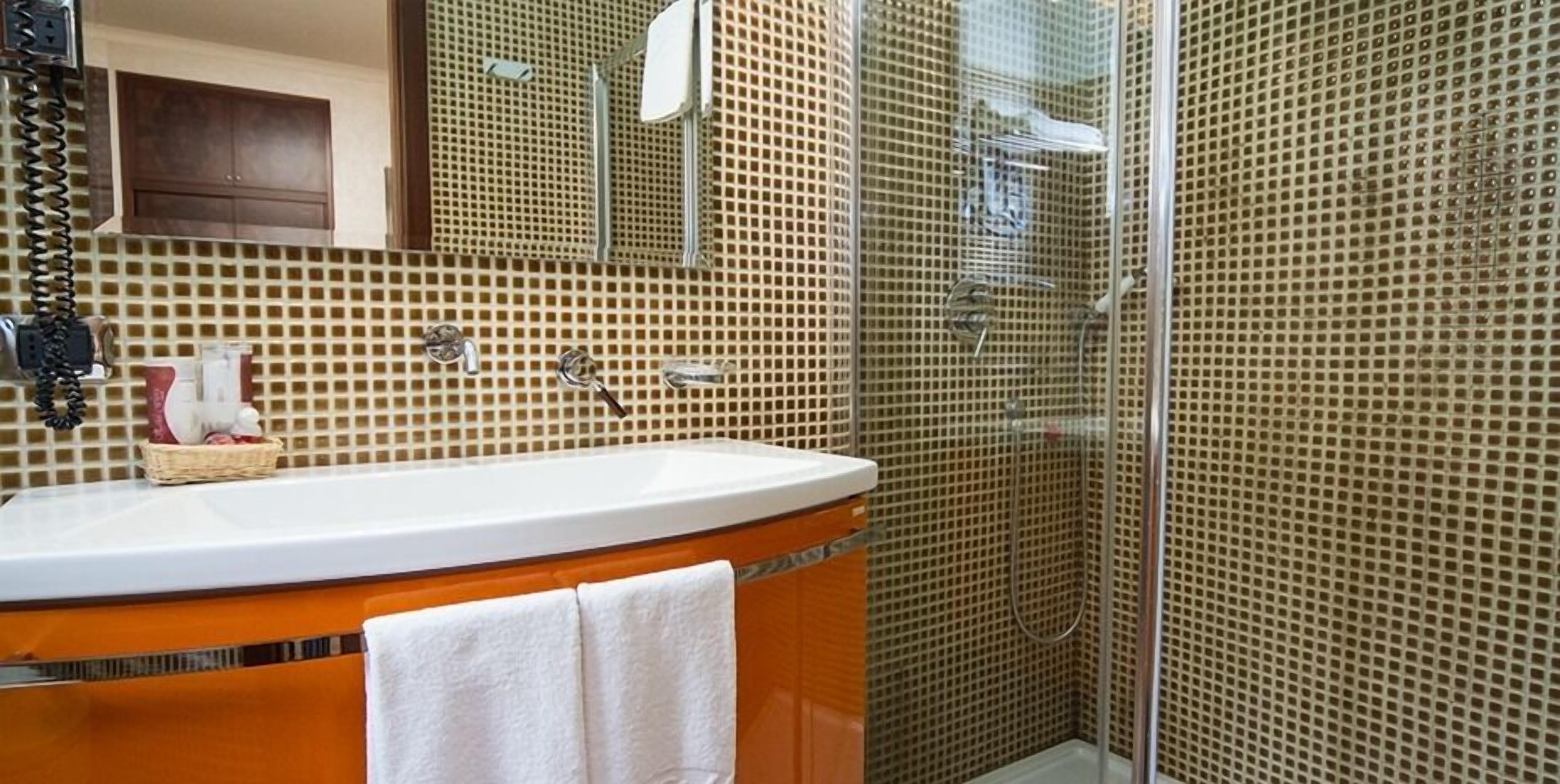 A bathroom with a sink, mirror, and shower area.