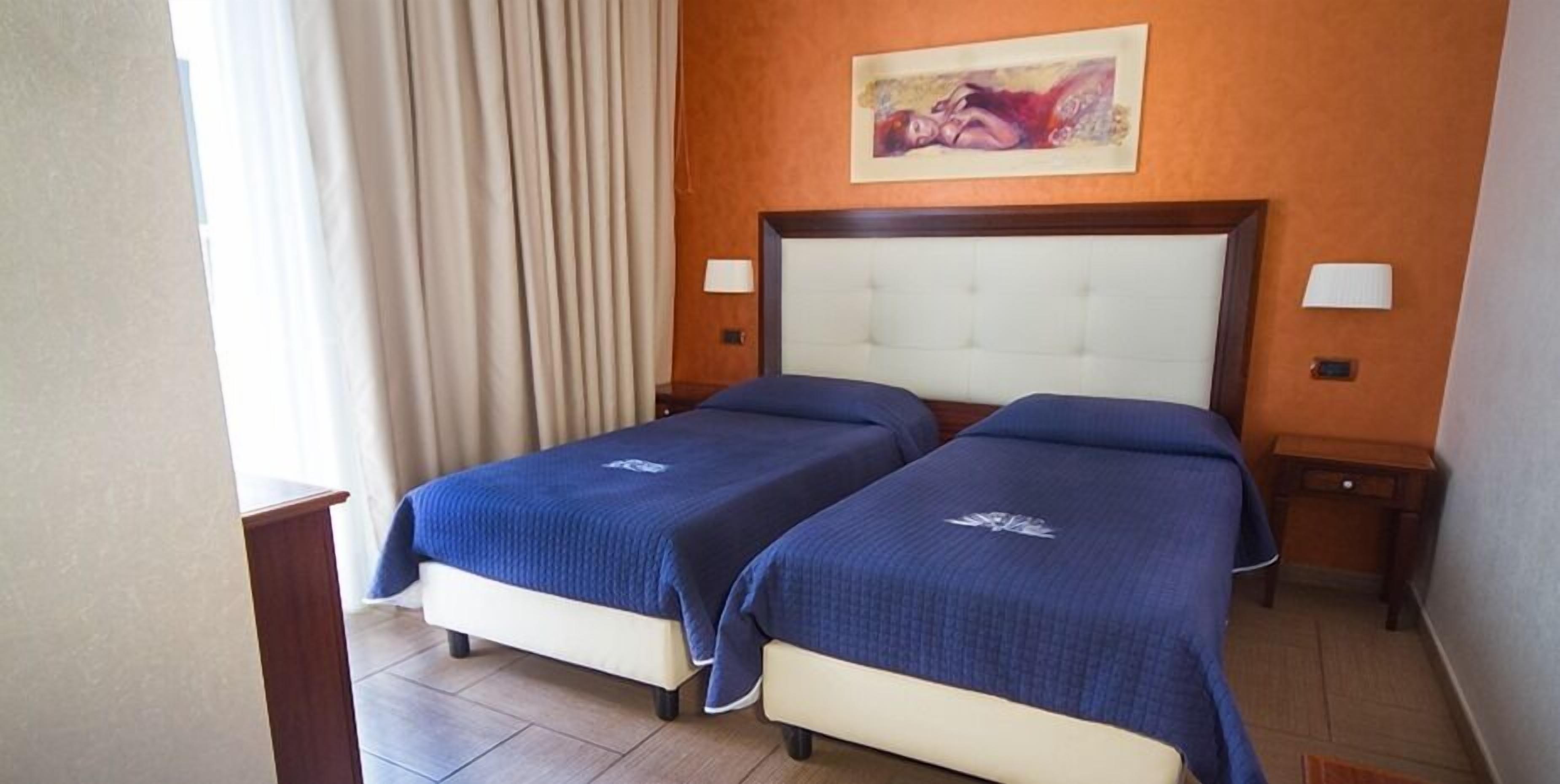 A hotel room with two beds, a large painting on the wall, and a window with curtains.