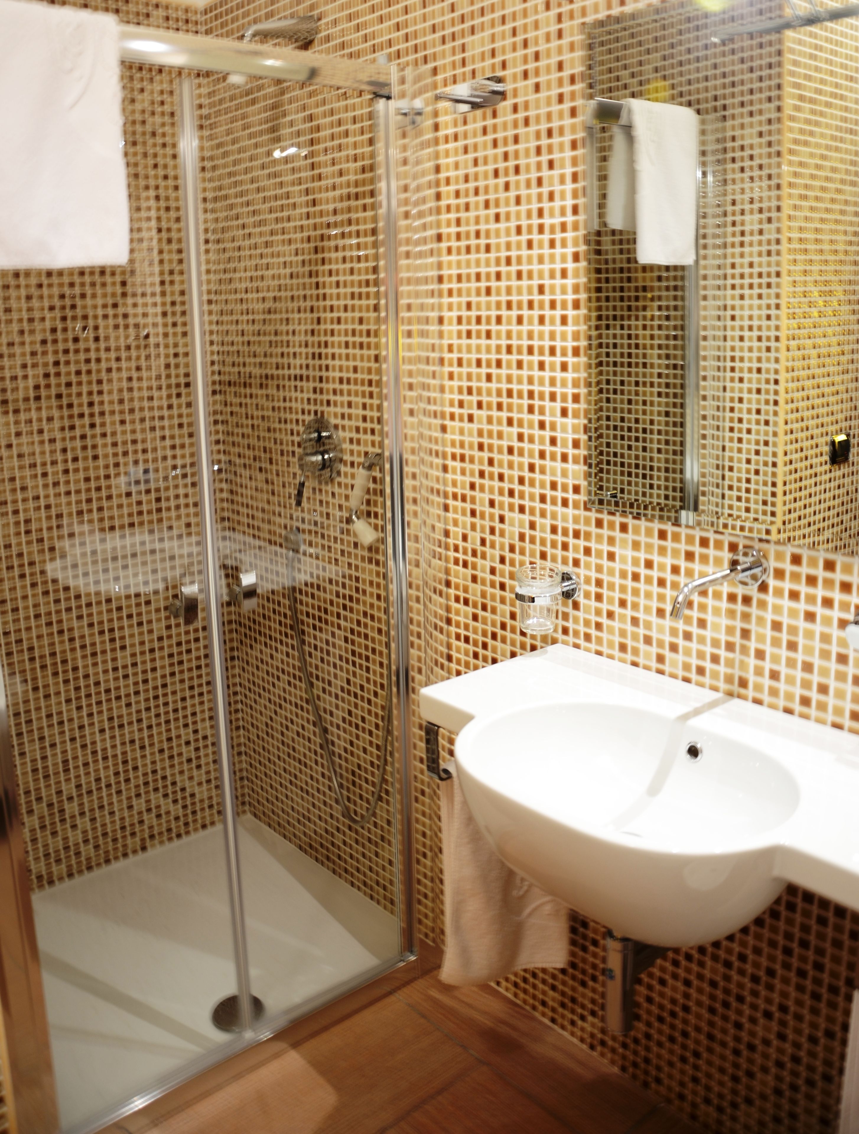 Een badkamer met een glazen douchecabine, een witte wastafel en een betegelde muur.