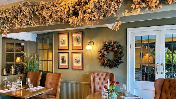 A dining area with a table set for four, a fireplace, and a wall adorned with framed artwork and a wreath. - The George Hotel Easingwold (York)