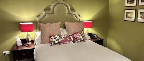 A neatly made bed with a headboard, two bedside tables with lamps, a telephone, and framed pictures on the wall.