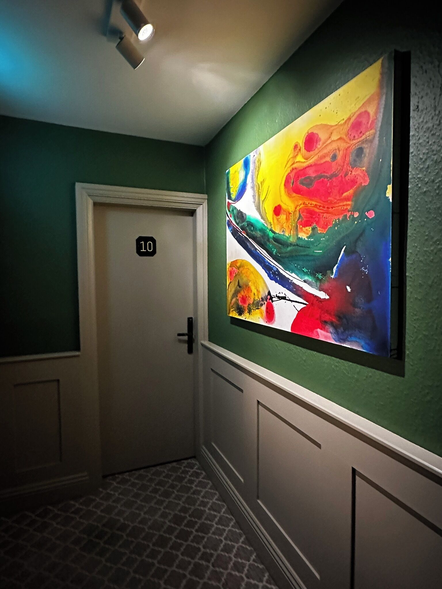 A hallway with a vibrant abstract painting on the wall, a door labeled '10', and a patterned floor.