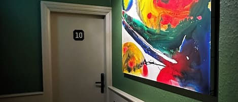A hallway with a vibrant abstract painting on the wall, a door labeled '10', and a patterned floor.