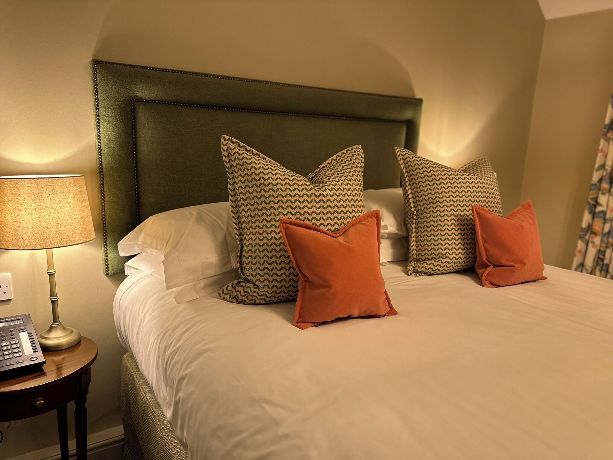 Una cama bien hecha con almohadas estampadas y una lámpara sobre una mesita de noche.