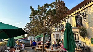 An outdoor seating area with wooden tables and green umbrellas, a bicycle parked by the building, and a sign for "The George Hotel". - The George Hotel Easingwold (York)