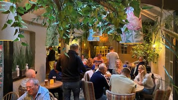 An indoor dining area with tables and chairs, surrounded by greenery and decorative elements.